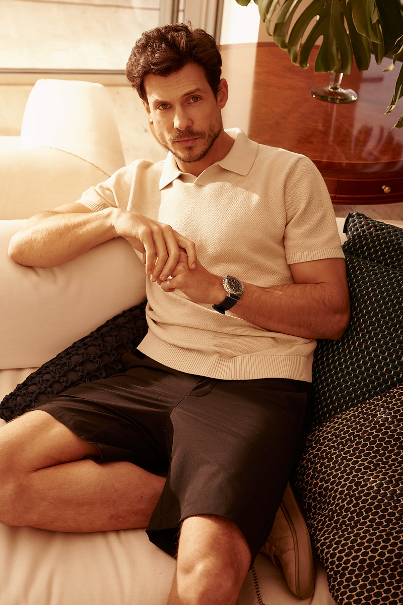 Homem sentado no sofá usando a Bermuda Everyday preta com polo de tricô bege